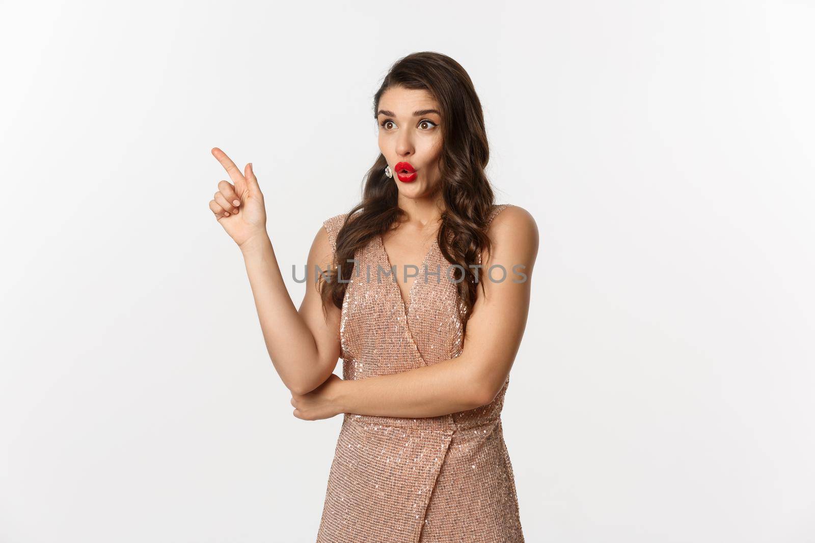 Christmas, holidays and celebration concept. Surprised girlfriend in evening dress, saying wow and pointing finger at promo offer, starring at logo, standing over white background.