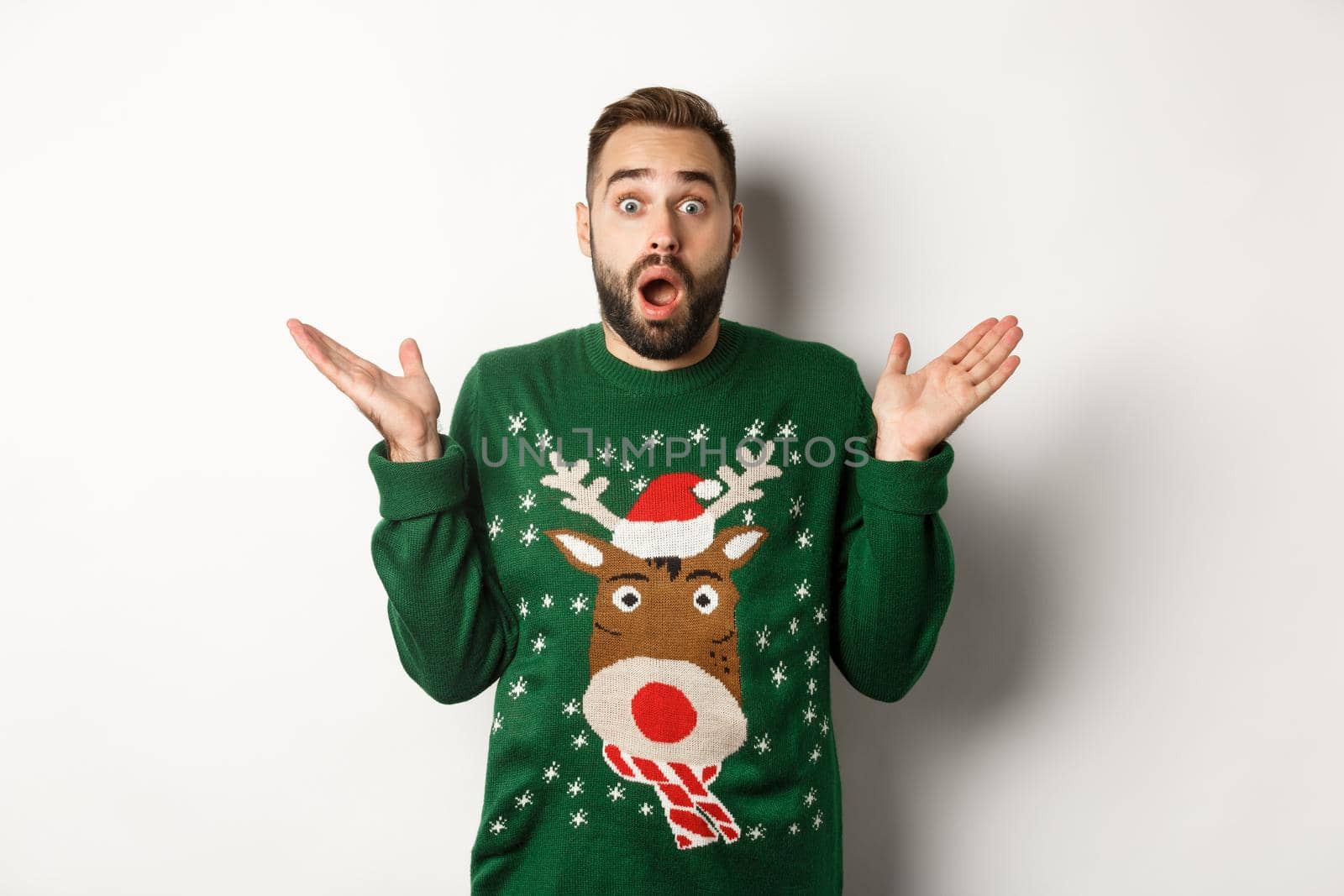 New Year party and winter holidays concept. Surprised bearded guy gasping amazed, standing in Christmas sweater, white background.