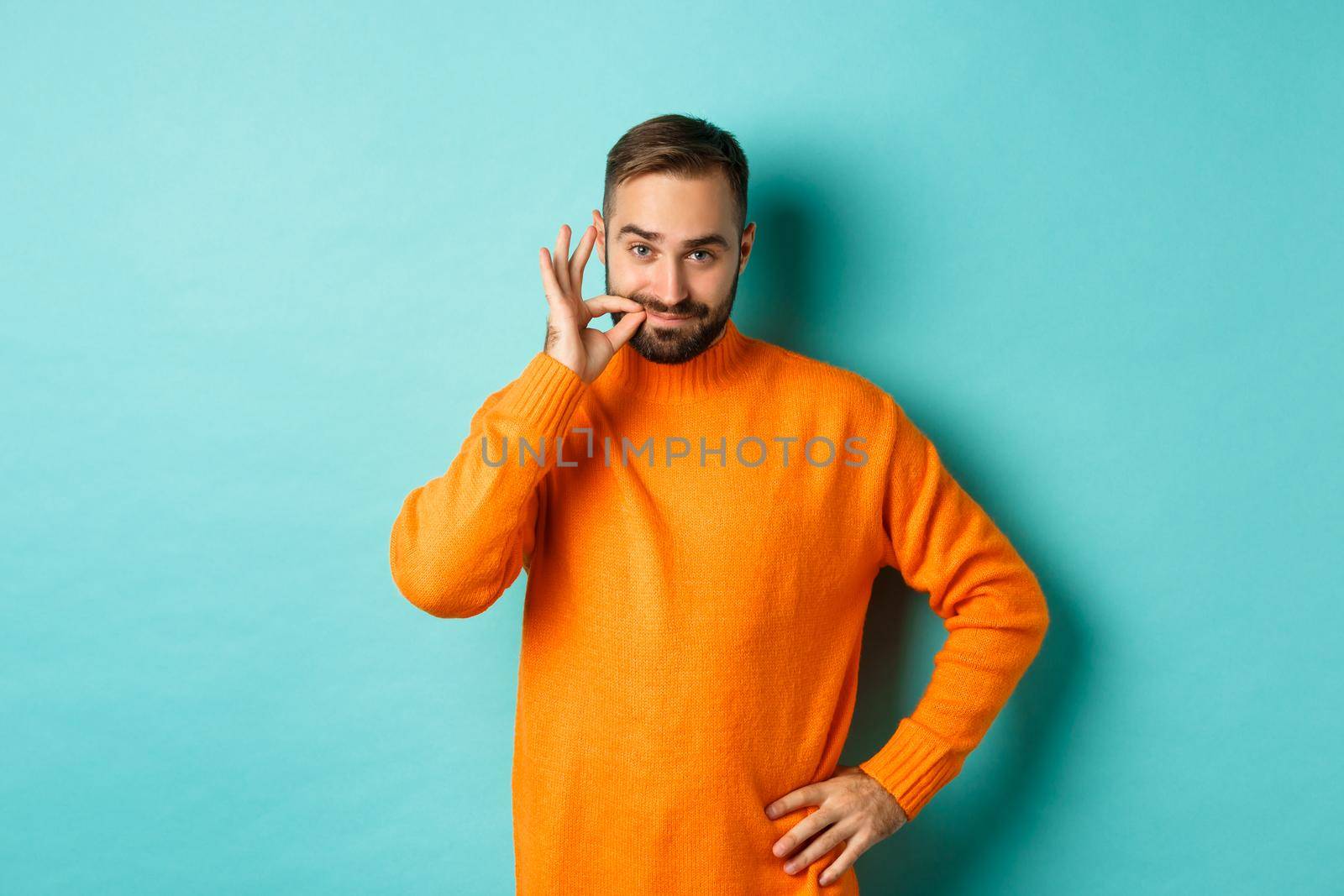 Handsome bearded man promise keep mouth shut, seal lips, lock mouth on key, standing over light blue background.