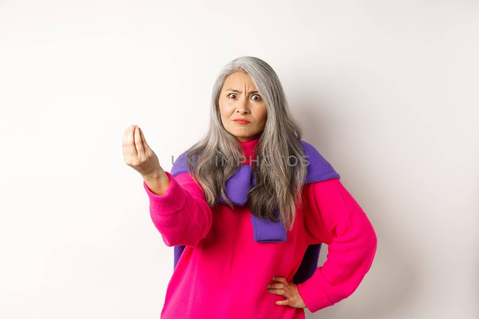 Funny asian woman staring angry and confused, shaking fingers, standing grumpy against white background by Benzoix