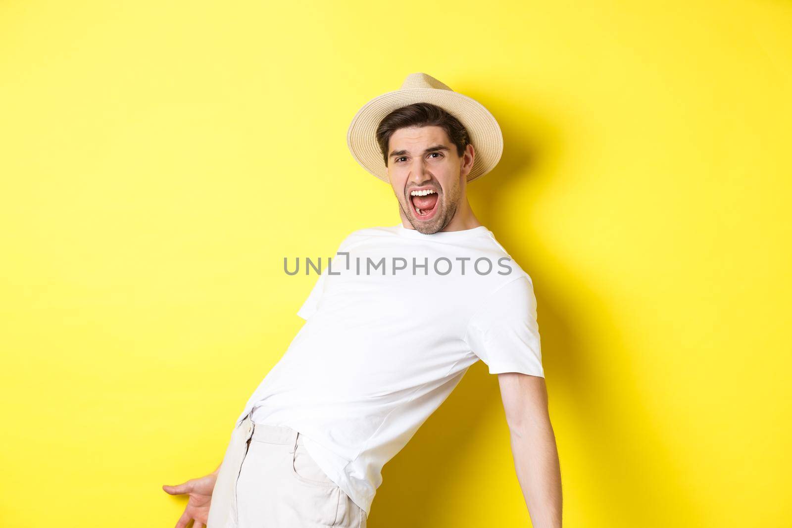 Concept of tourism and vacation. Excited young man tourist celebrating, shouting for joy and dancing, standing over yellow background.