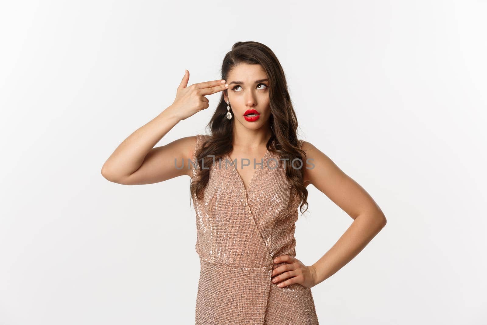 Celebration and party concept. Annoyed woman in elegant evening dress wants to kill herself from boredom, shooting finger gun in head and roll eyes irritated, standing over white background.