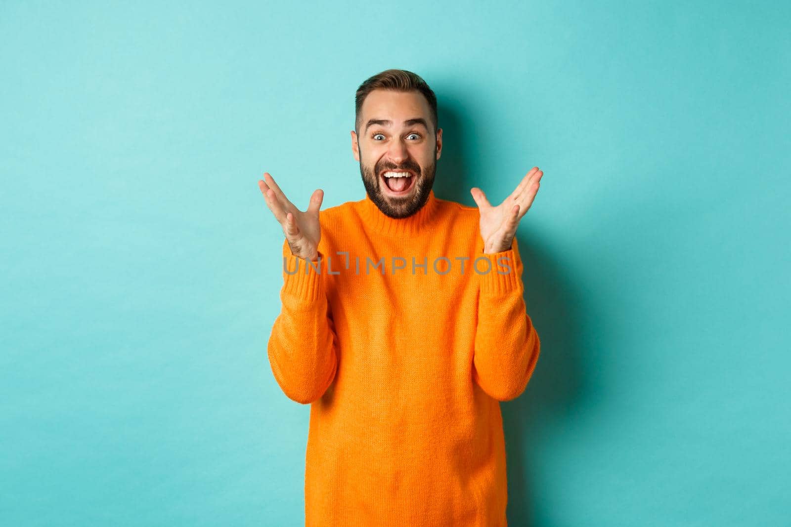 Image of excited and happy bearded man, shaking hands and smiling amazed, telling big news, standing over light blue background.