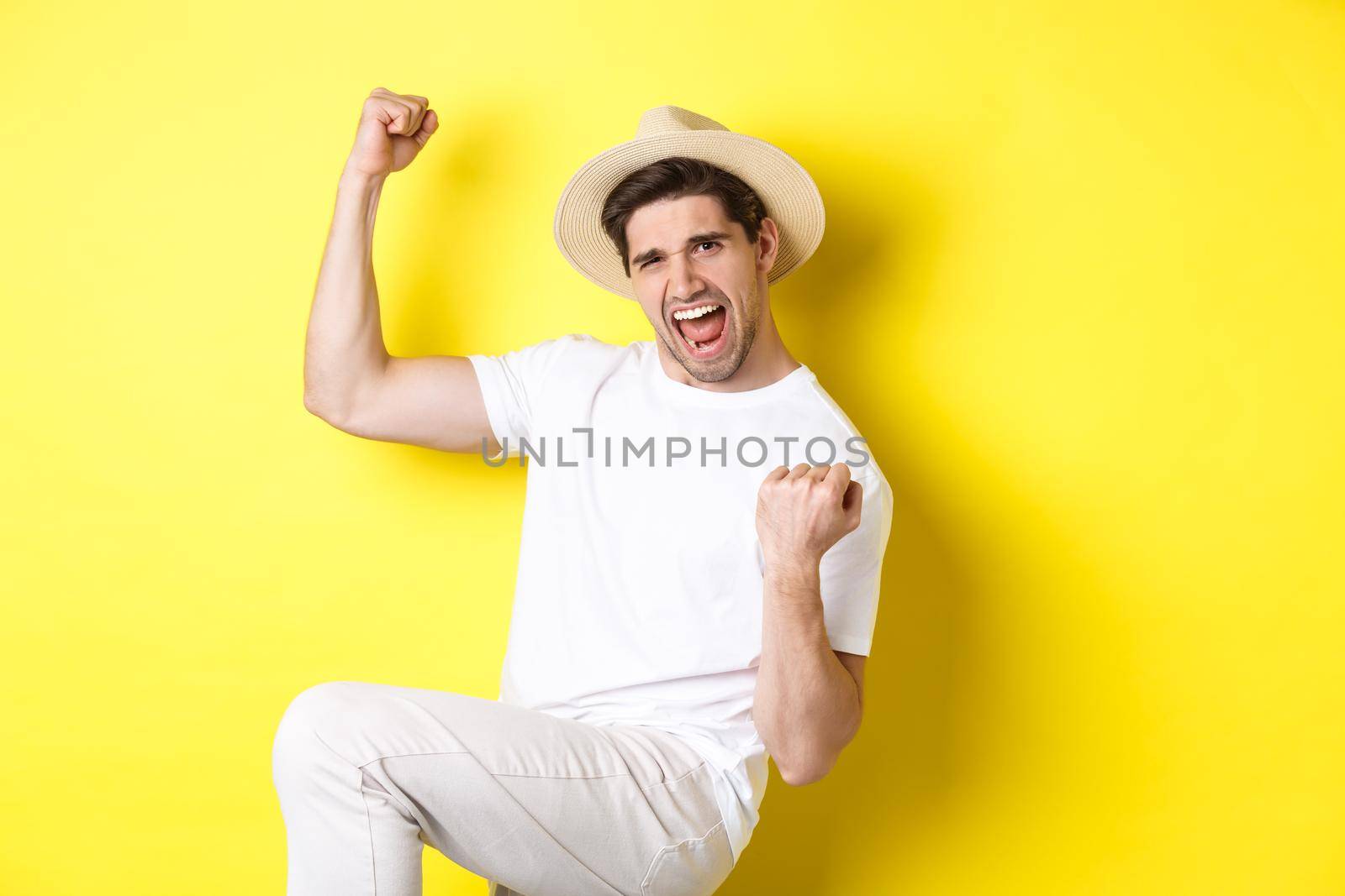 Concept of tourism and vacation. Lucky male tourist winning trip, rejoicing and saying yes, making fist pump while triumphing, standing against yellow background.