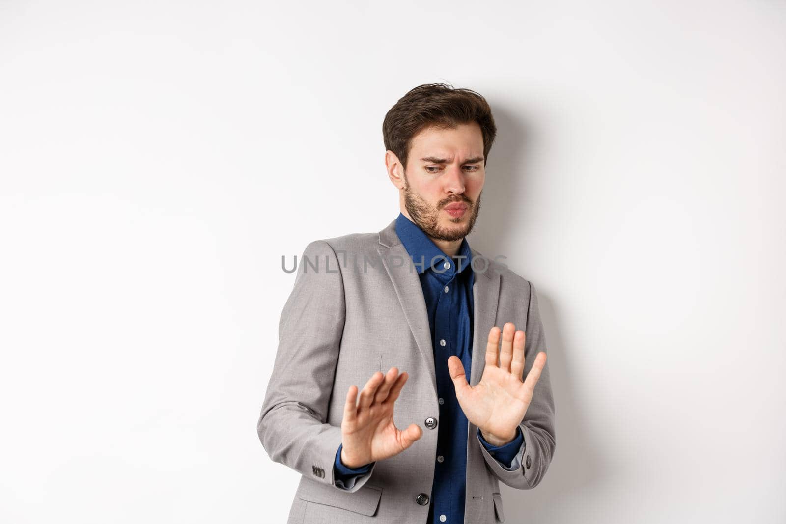 Stay away. Reluctant businessman step back with concerned disgusted face, raising hands to block bad offer, rejecting something awful, tilting from disgust, white background.