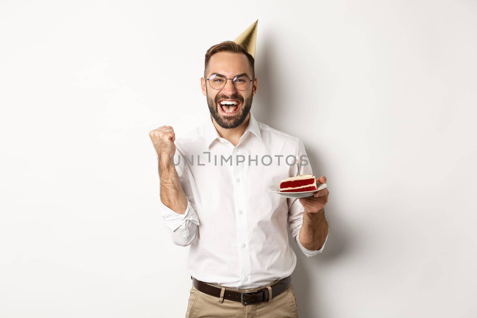 Holidays and celebration. Birthday guy making wish on bday cake and rejoicing, making fist pump sign as winning, achieve goal, white background.