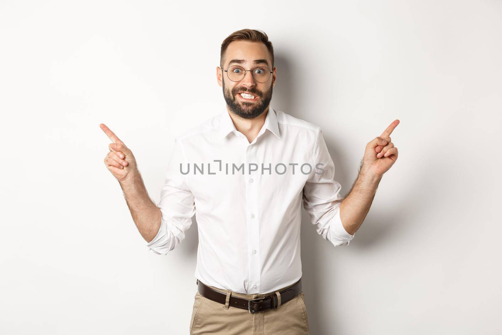 Indecisive businessman pointing sideways, showing two variants, struggling make choice, standing over white background.