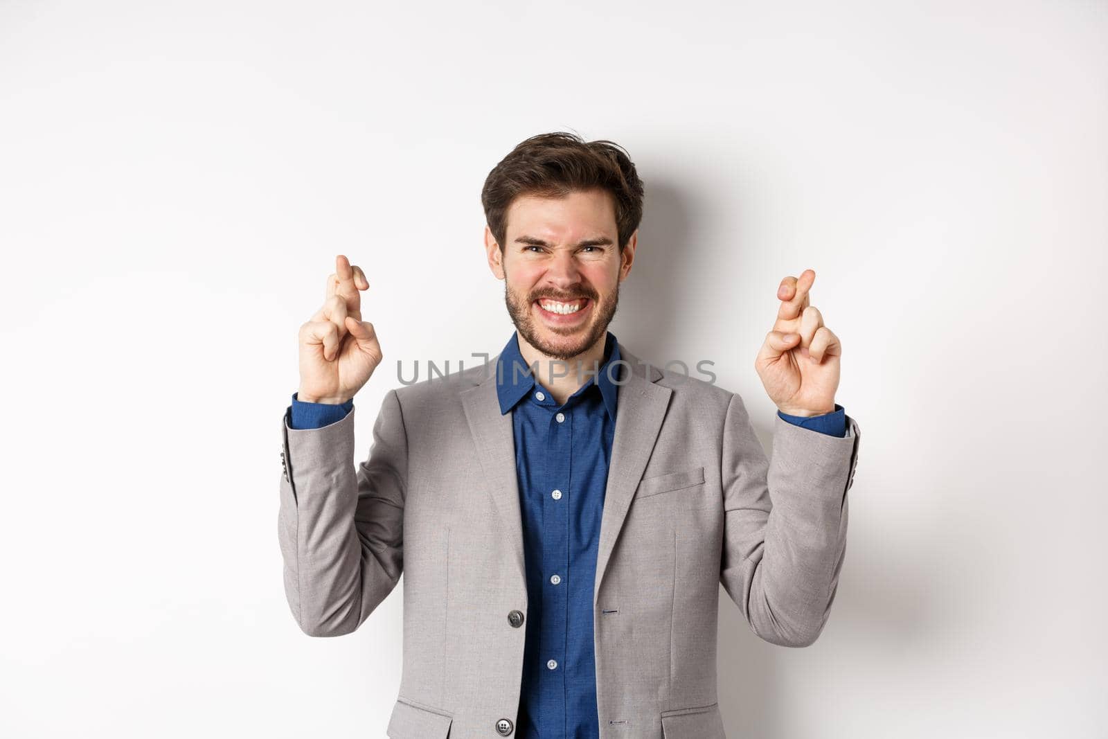 Motivated and excited businessman smiling positive, look hopeful and cross fingers for good luck, making wish, waiting for announcement, white background.