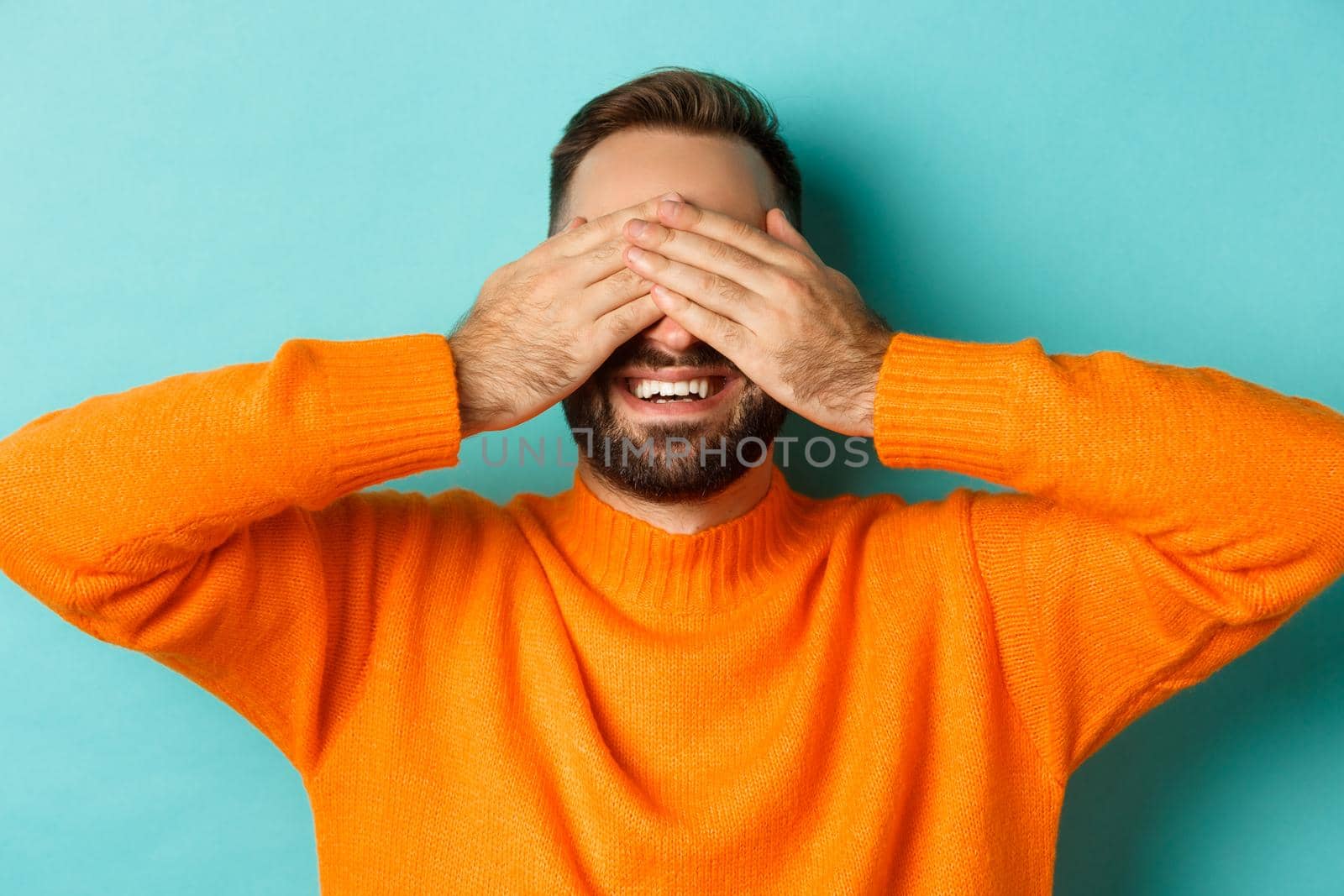 Close-up of happy caucasian man waiting for surprise, close eyes and smiling, standing over light bue background.