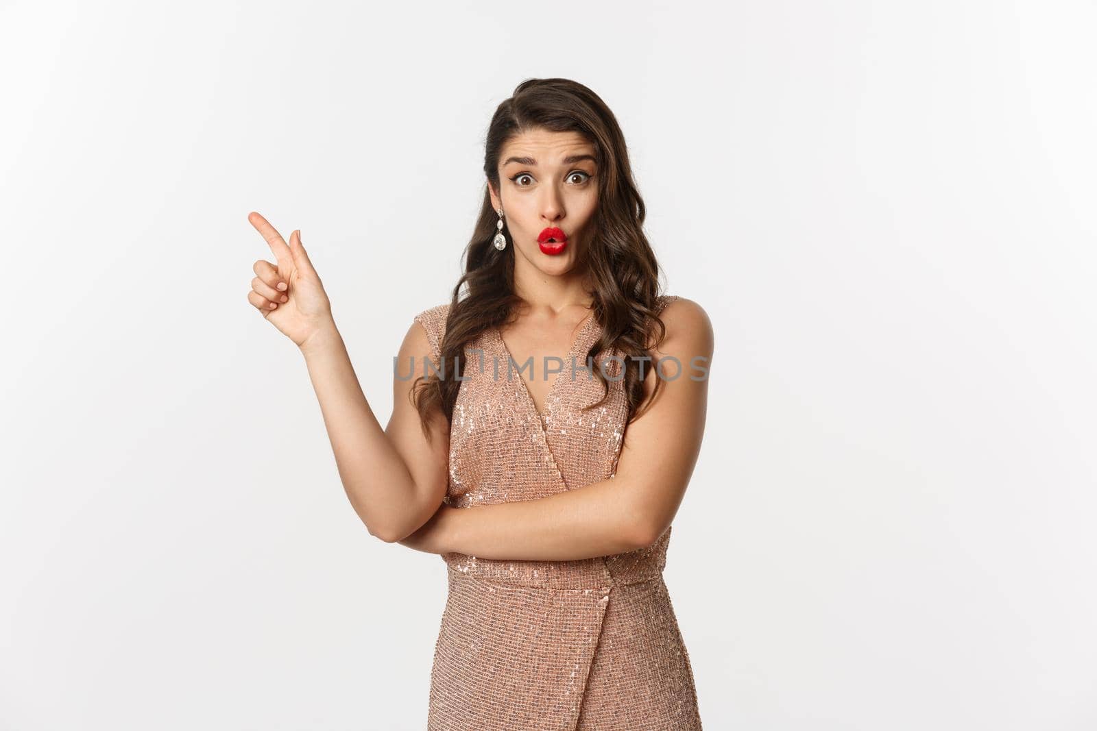 Christmas, holidays and celebration concept. Intrigued beautiful woman asking question about promo offer, pointing finger left at logo or banner, standing in party dress.
