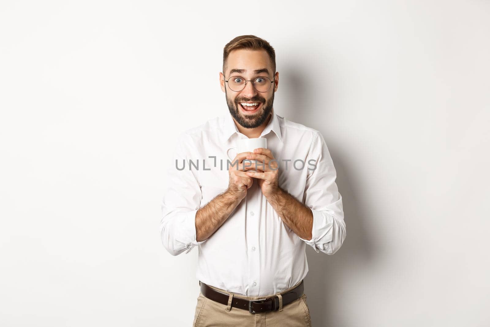 Man drinking coffee and looking excited, enjoying drink, standing over white background.