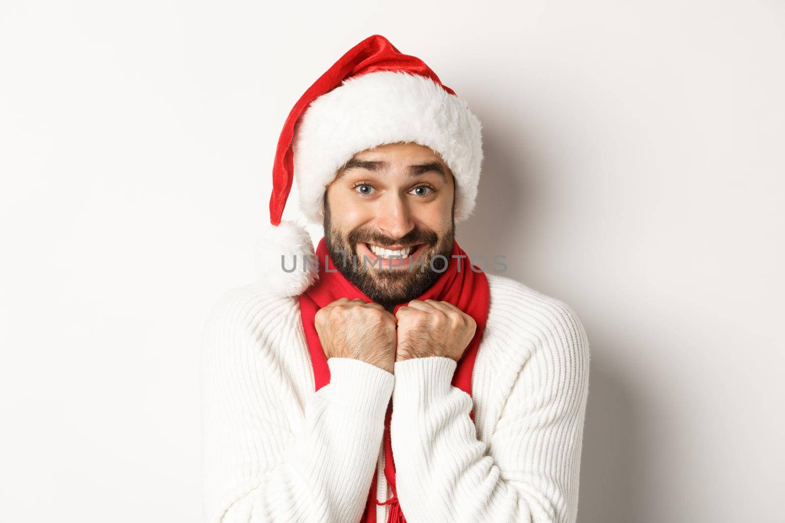 New Year party and winter holidays concept. Handsome guy in Santa hat feeling excited about Christmas, standing amused against white background by Benzoix