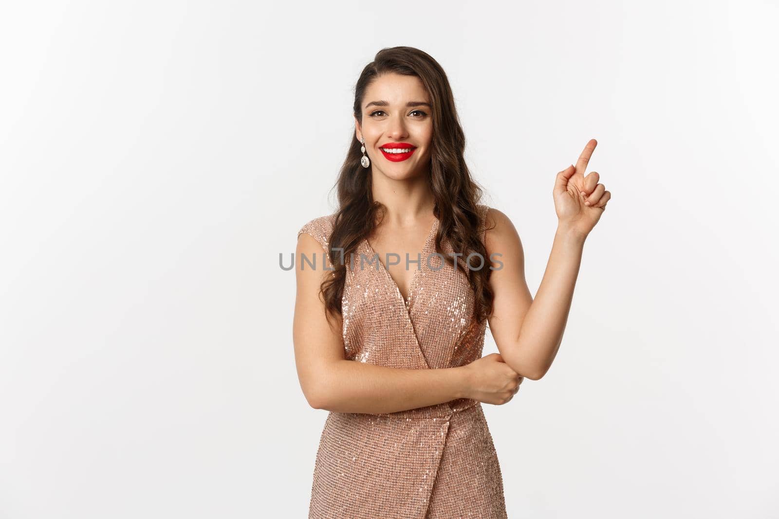 Beautiful woman in elegant dress on christmas party, pointing finger right at logo, smiling with red lips, standing over white background.