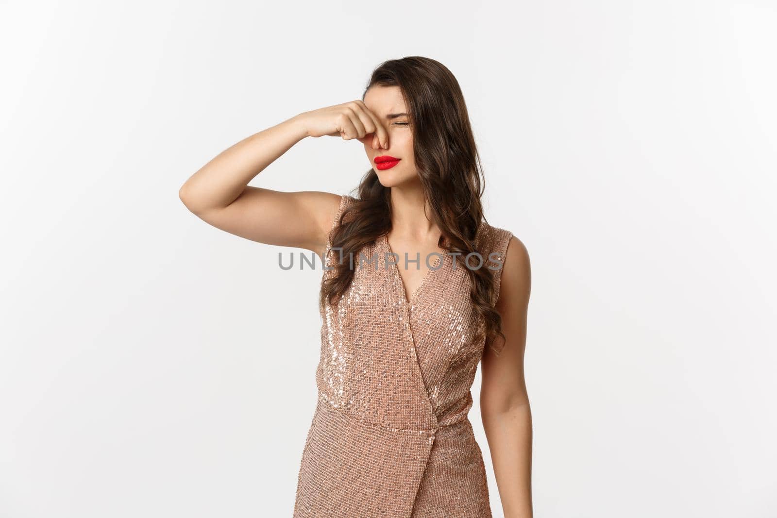 Attractive young woman with red lips, glamour dress, shut nose with fingers from disgusting smell, something reek, standing over white background.