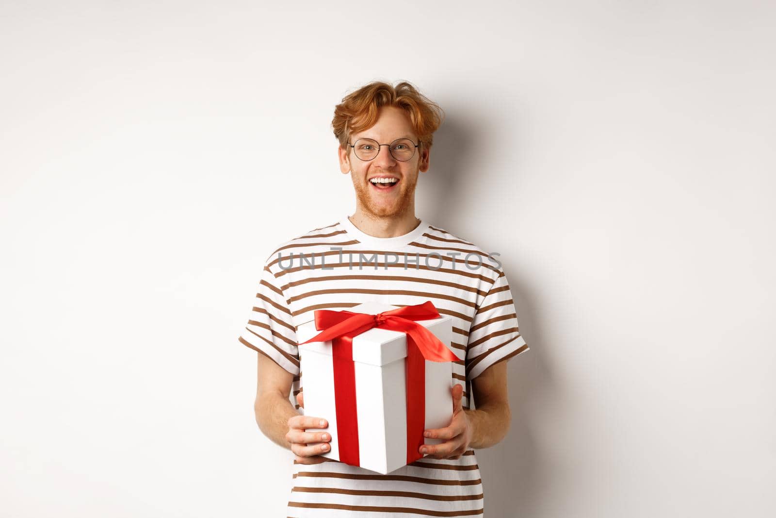 Valentines day and holidays concept. Cheerful young man holding gift box and smiling grateful, receiving presents, standing over white background.