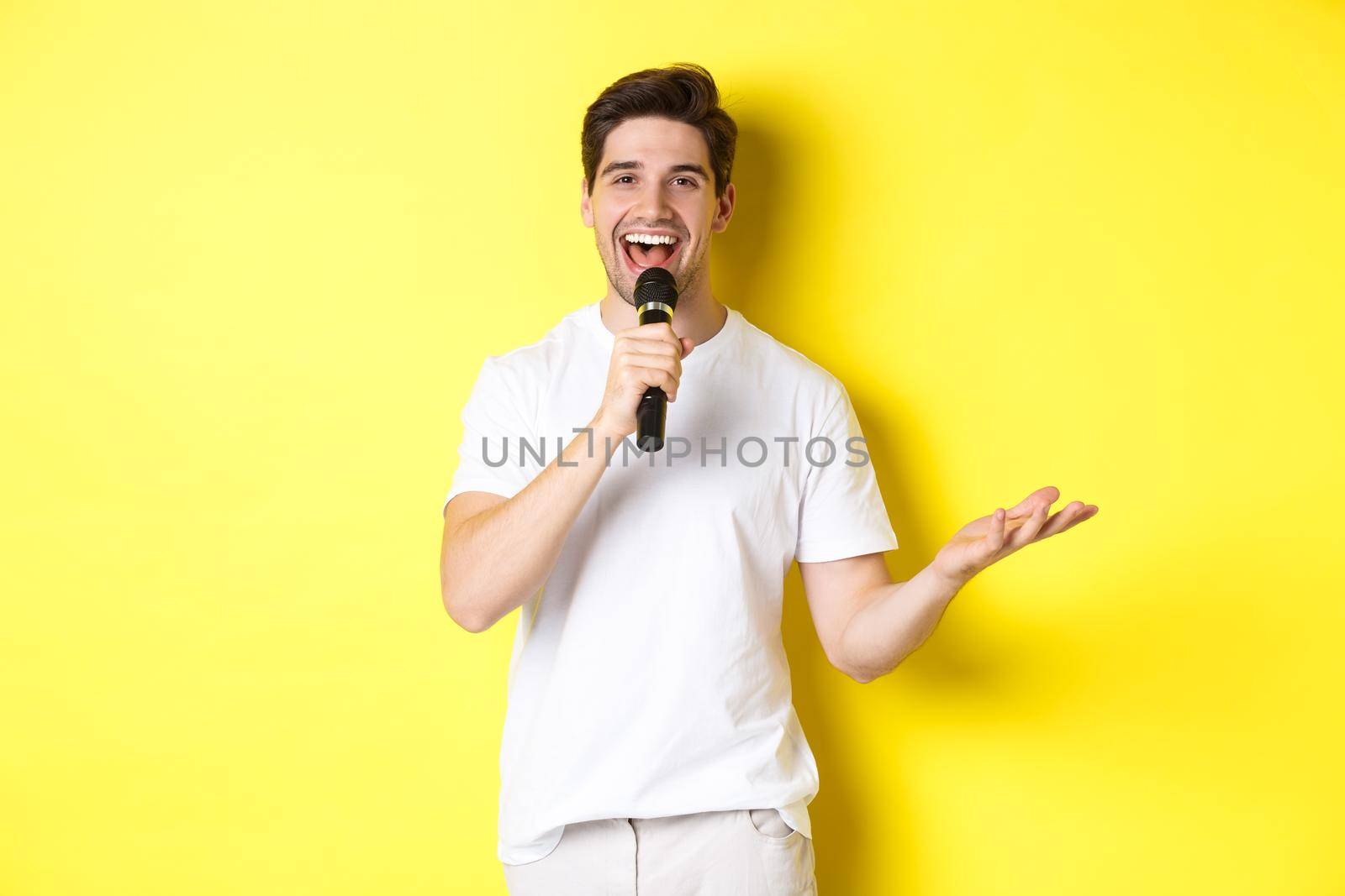 Happy man entertainer performing, talking in microphone, making speech or stand-up show, standing over yellow background by Benzoix