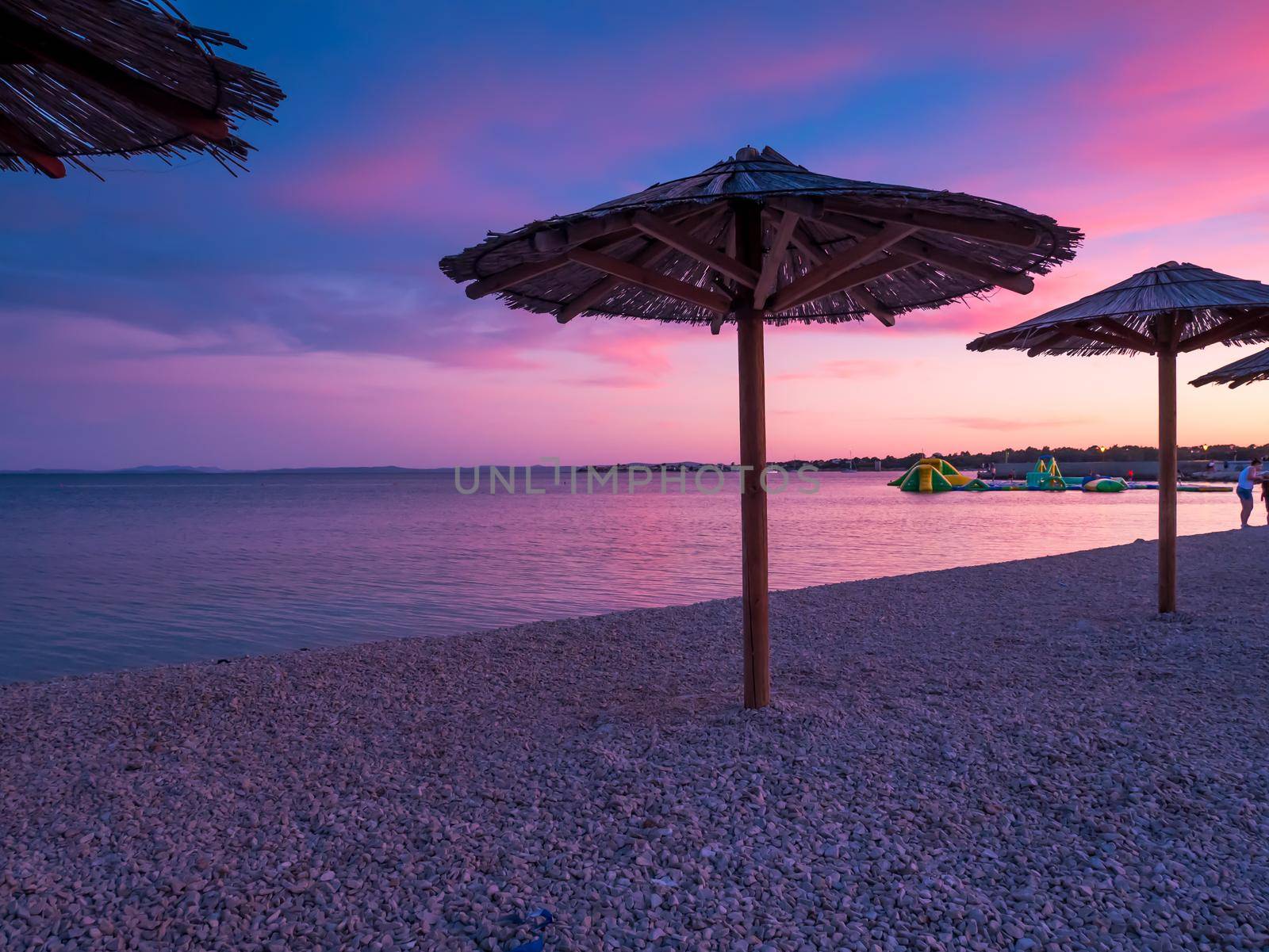 Beach umbrellas, view of the beautiful blue and purple sunset, sky and straw beach umbrellas. Perfect holiday concept. Travel and vacation. Beach on Vir Island, Croatia, Europa. Copy space.