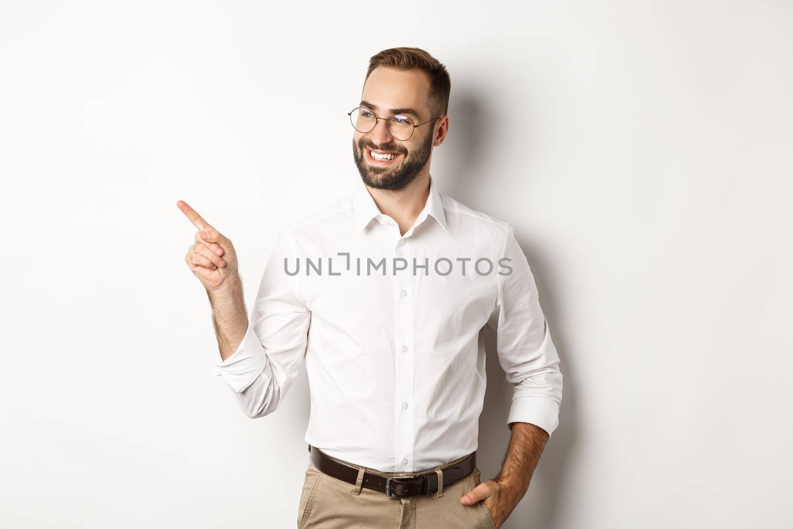 Confident businessman looking satisfied and pointing finger left, showing company banner, standing over white background.
