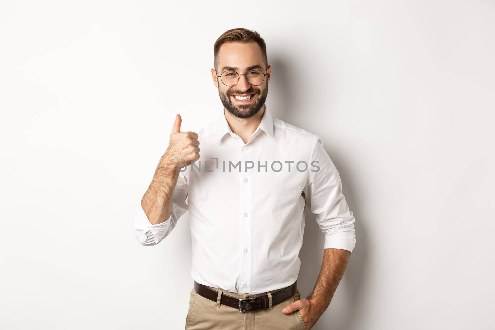 Satisfied successful boss showing thumb up, approve and praise good work, standing over white background.