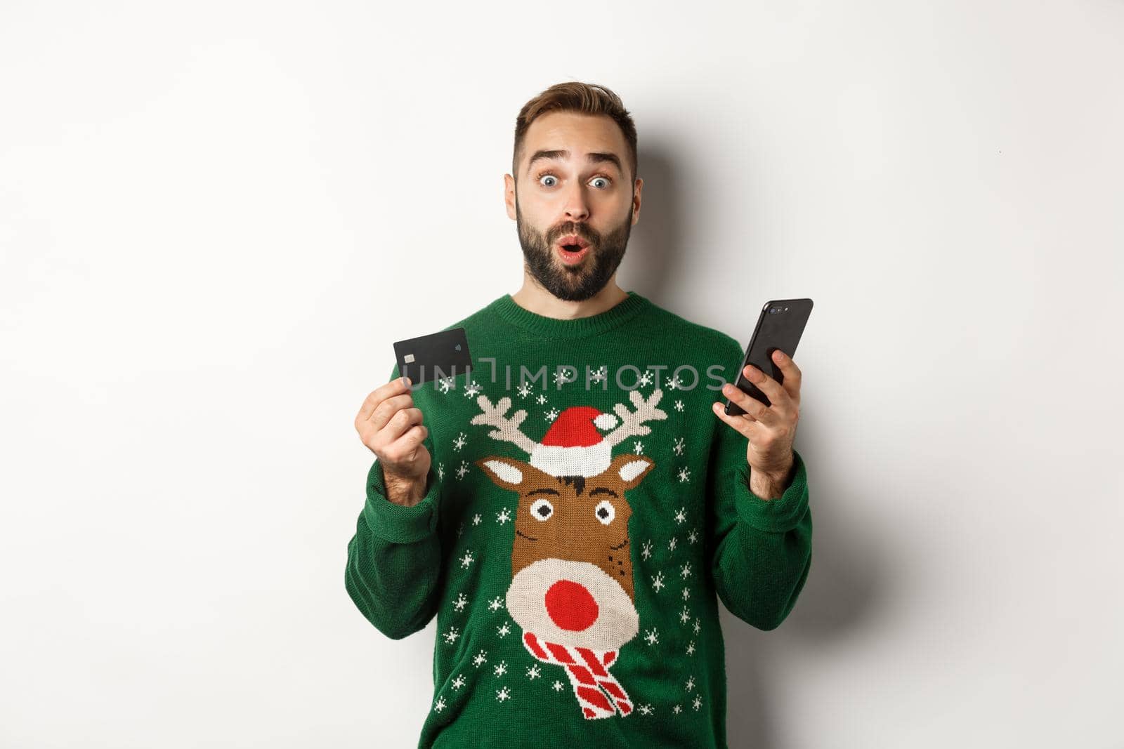New Year, online shopping and christmas concept. Excited man using credit card and smartphone, standing over white background.