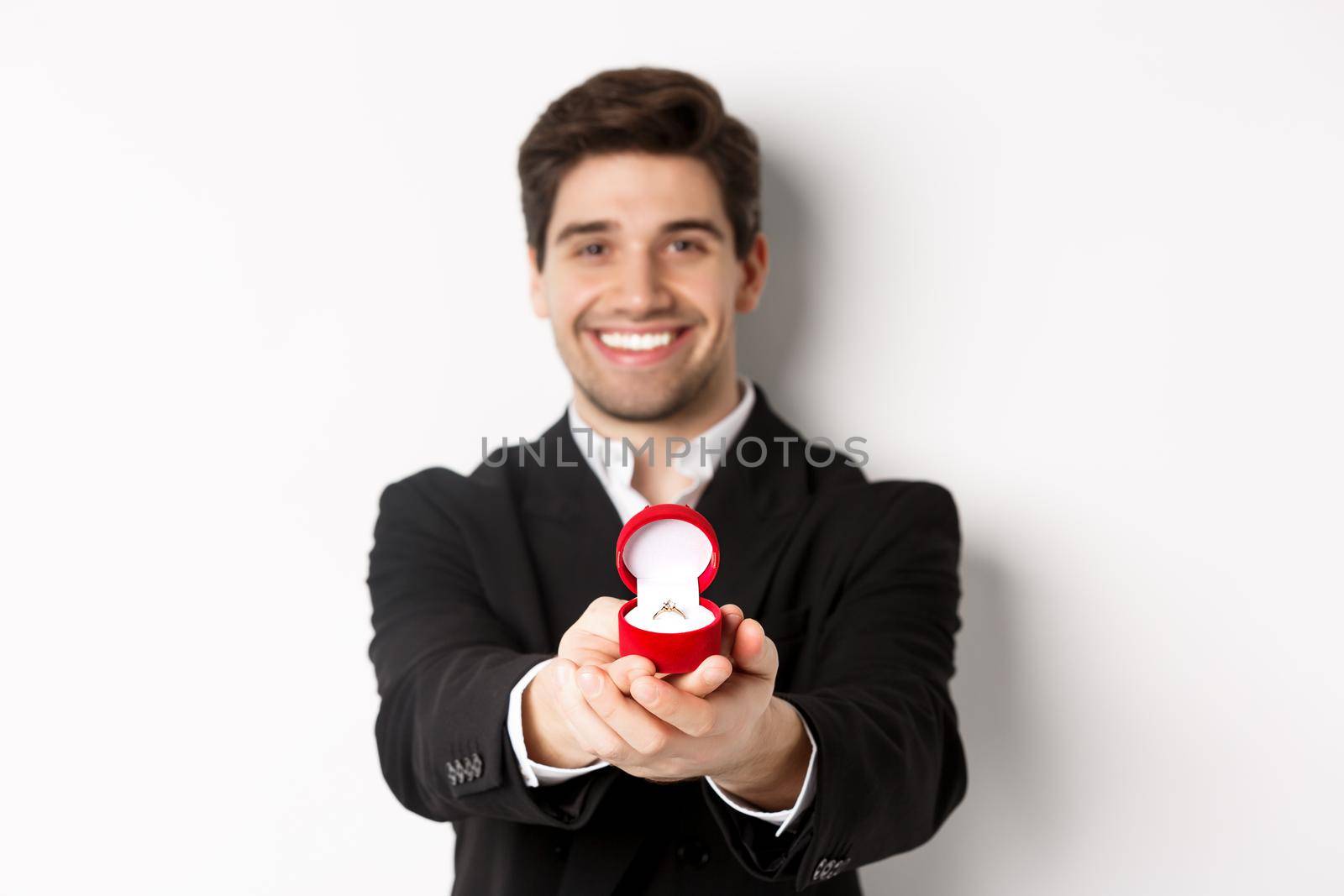 Image of handsome man looking romantic, giving you an engagement ring, making proposal to marry him, standing against white background by Benzoix
