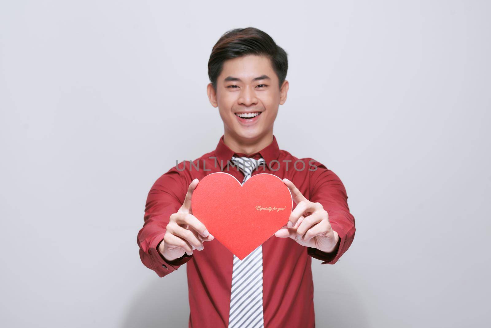 Cute handsome asian holds out a red heart made of paper for Valentine's Day on a white background with copy space by makidotvn