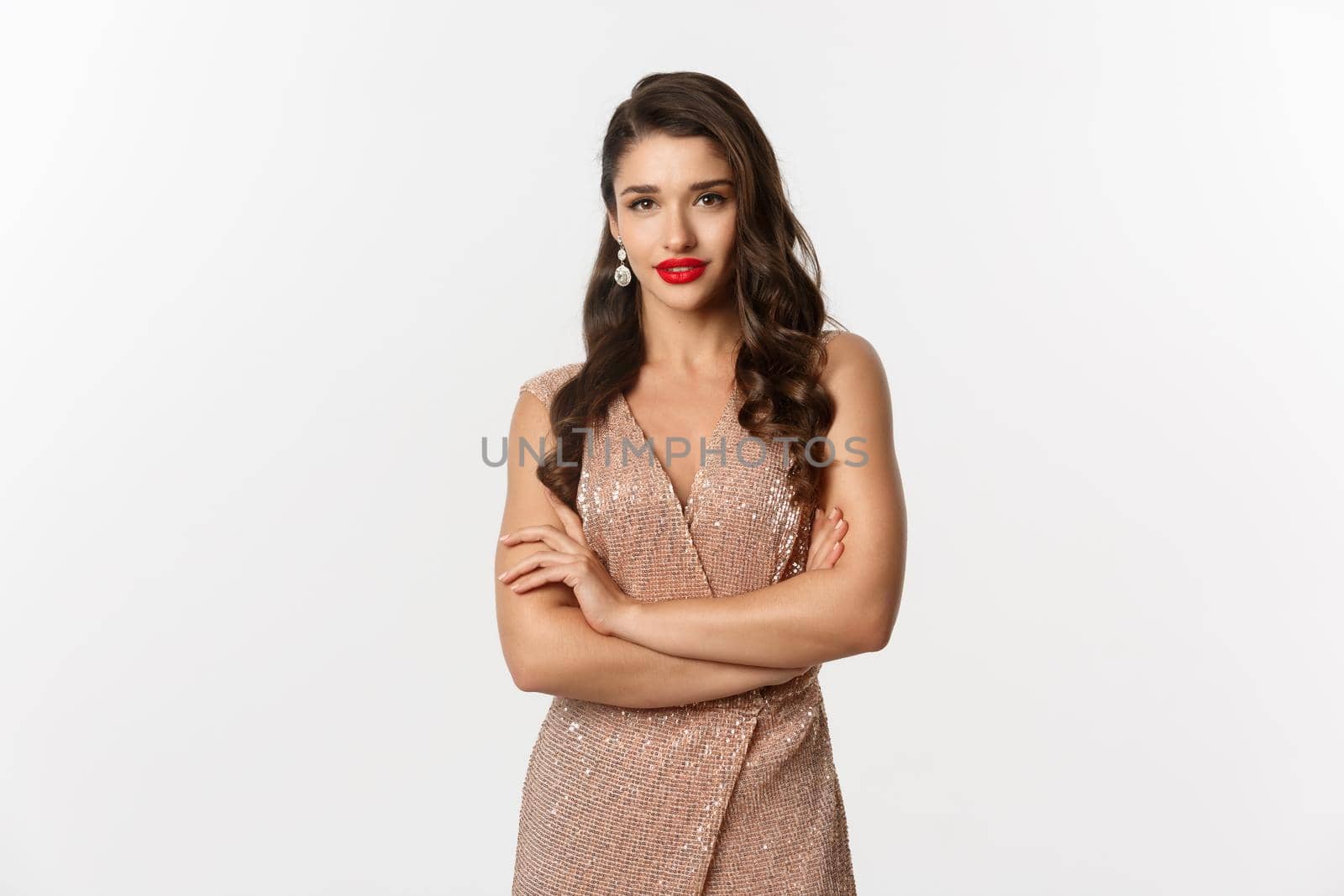 Celebration. Elegant woman in party dress and makeup, wearing red lipstick, looking confident at camera, cross arms on chest, white background.