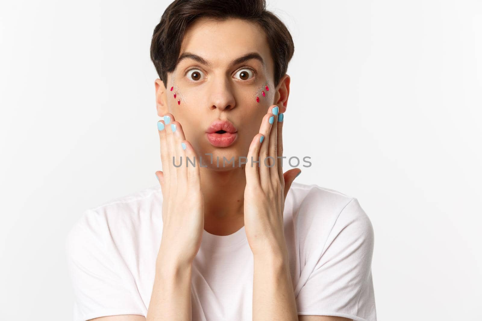 People, lgbtq and beauty concept. Close-up of handsome gay man express surprise, showing hands with blue nail polish, standing over white background.