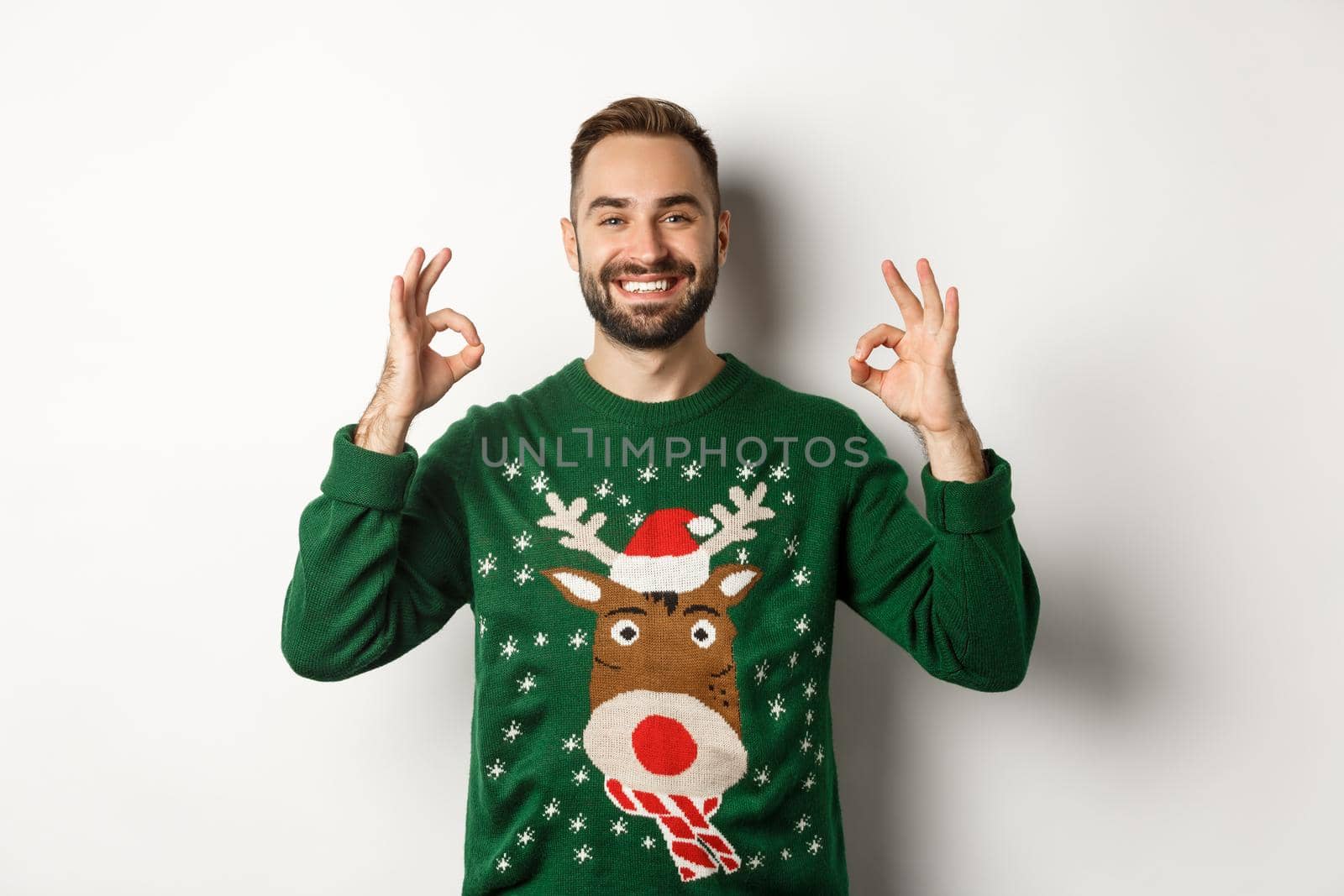 Christmas, holidays and celebration. Satisfied smiling man in green sweater showing OK signs and nodding in approval, recommending product, standing over white background.