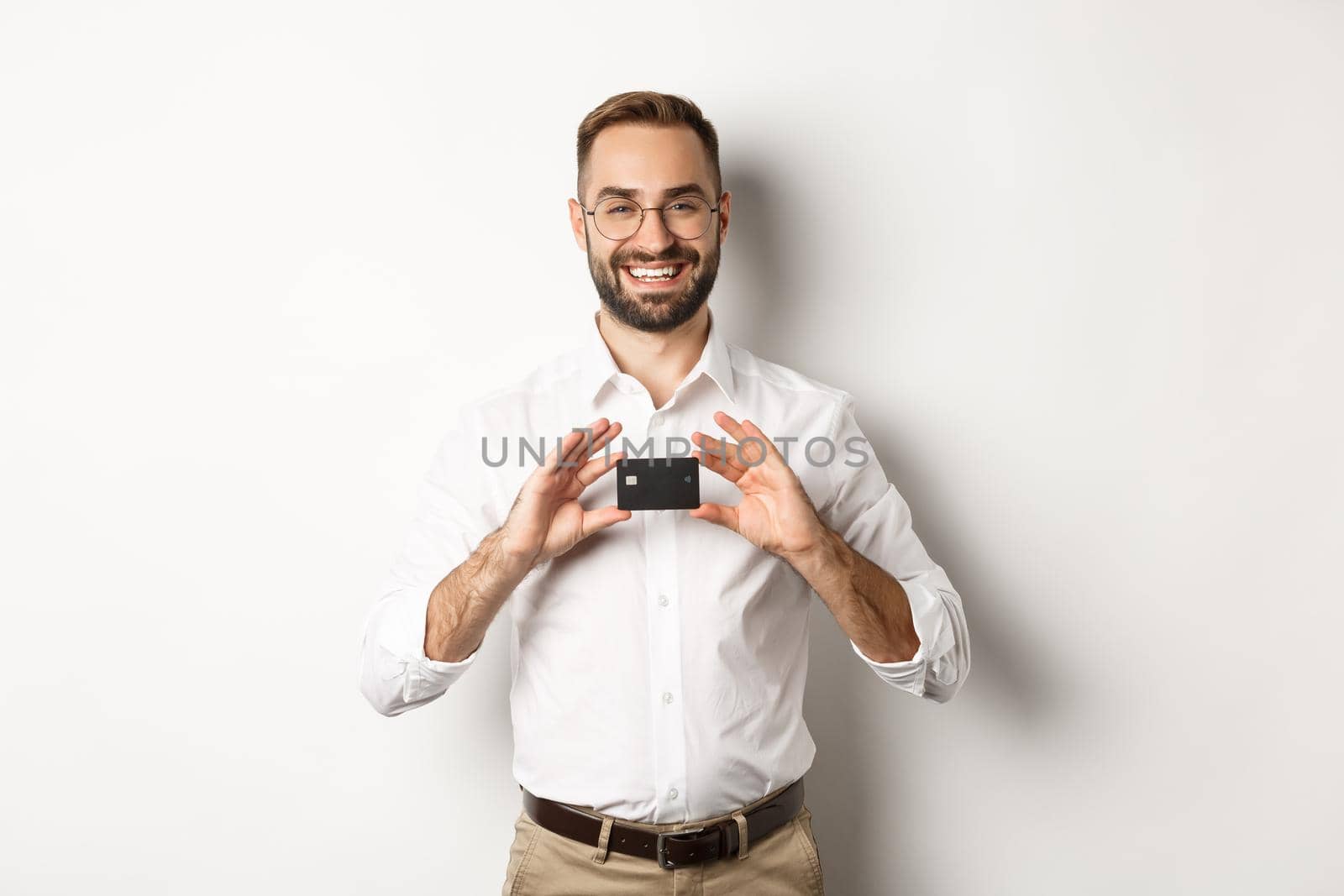 Handsome businessman holding a card, smiling satisfied, standing over white background.