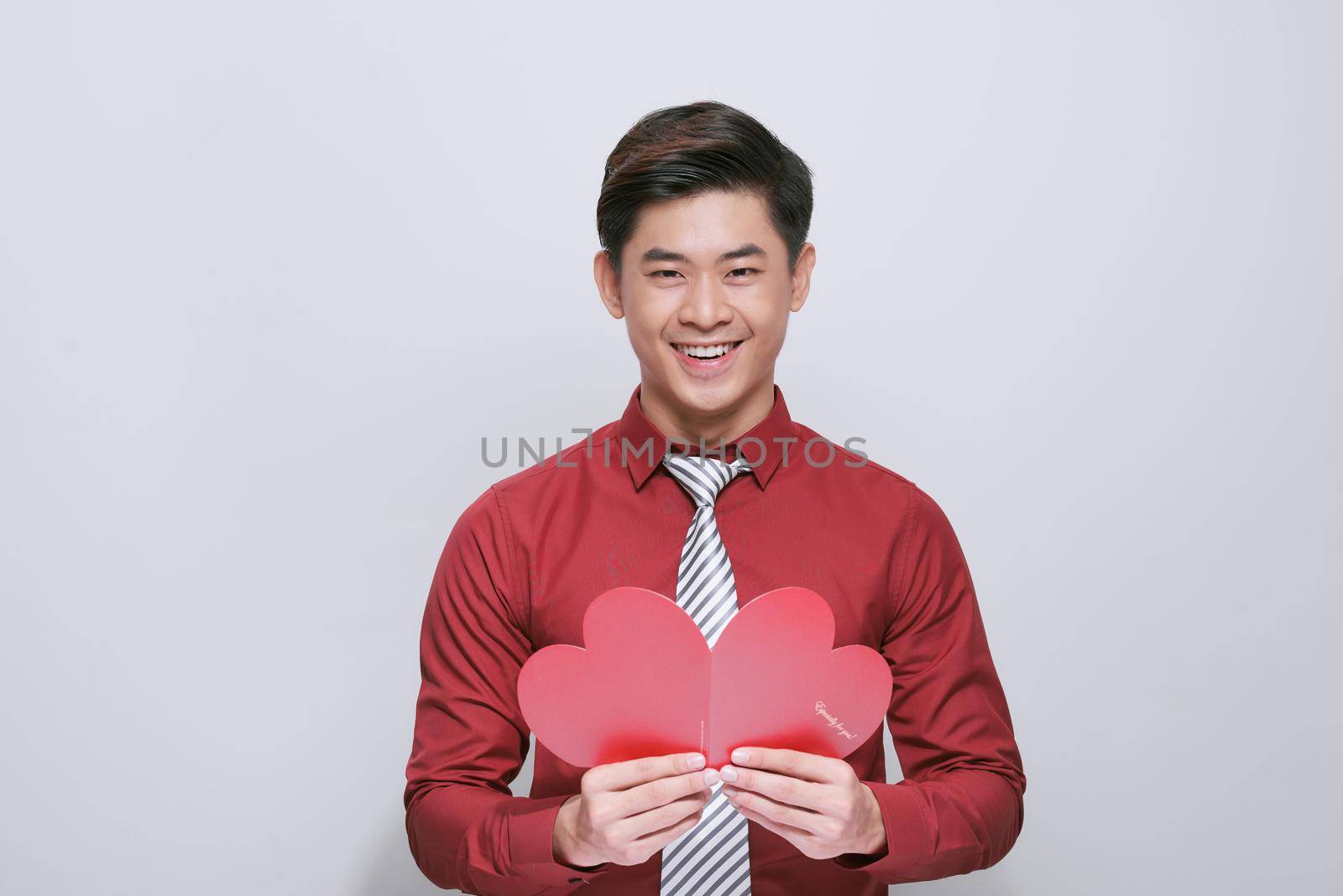 Handsome man with greeting card on light background. Valentine's Day celebration