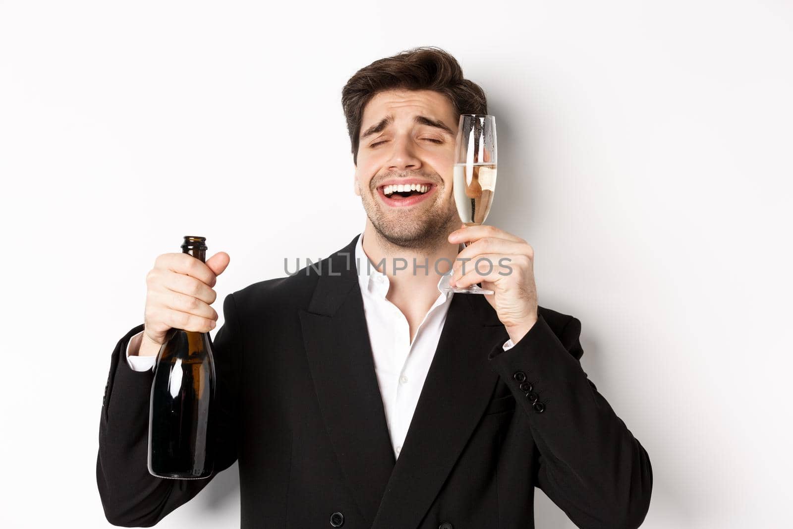 Close-up of handsome drunk guy in suit, holding glass of champagne and celebrating new year, standing over white background by Benzoix