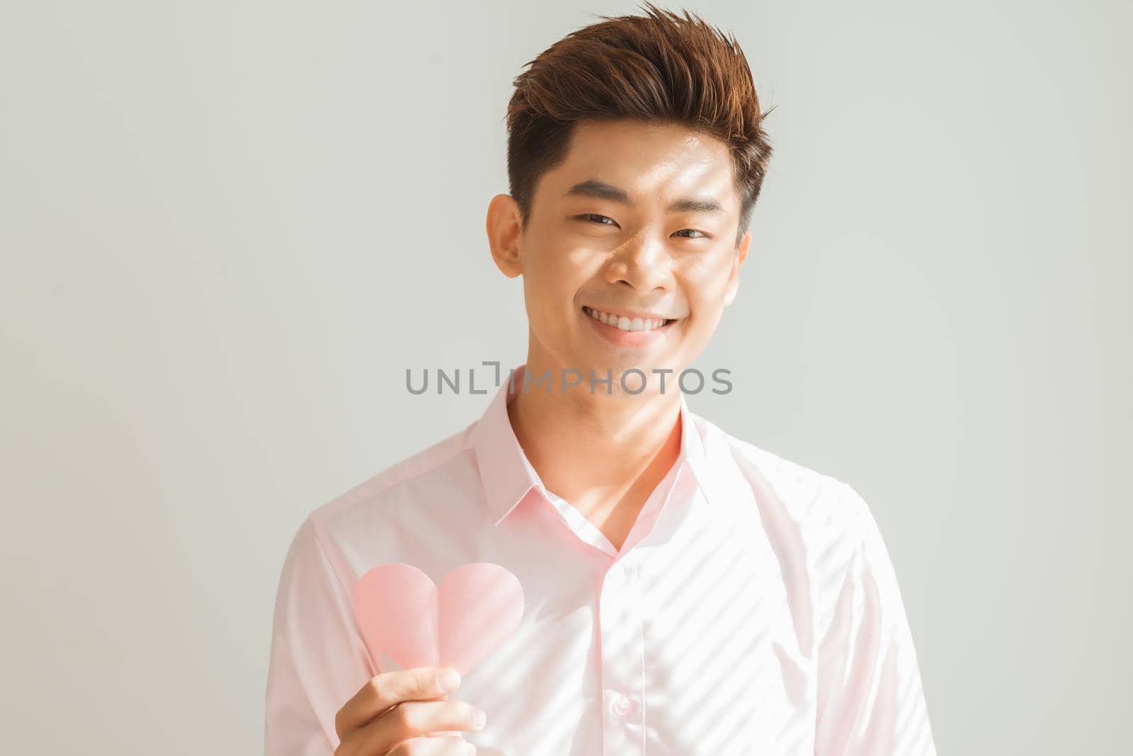 Portrait of tender gentle romantic sweet lovely open-hearted man showing pink heart in hands isolated on white background by makidotvn