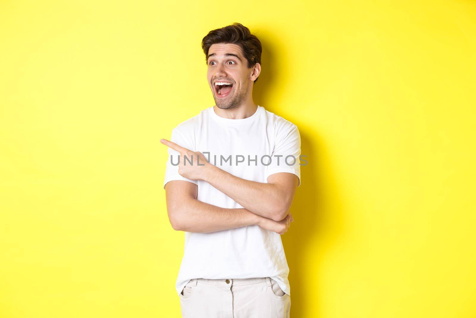Excited smiling man pointing and looking left, checking out promo offer, standing over yellow background.