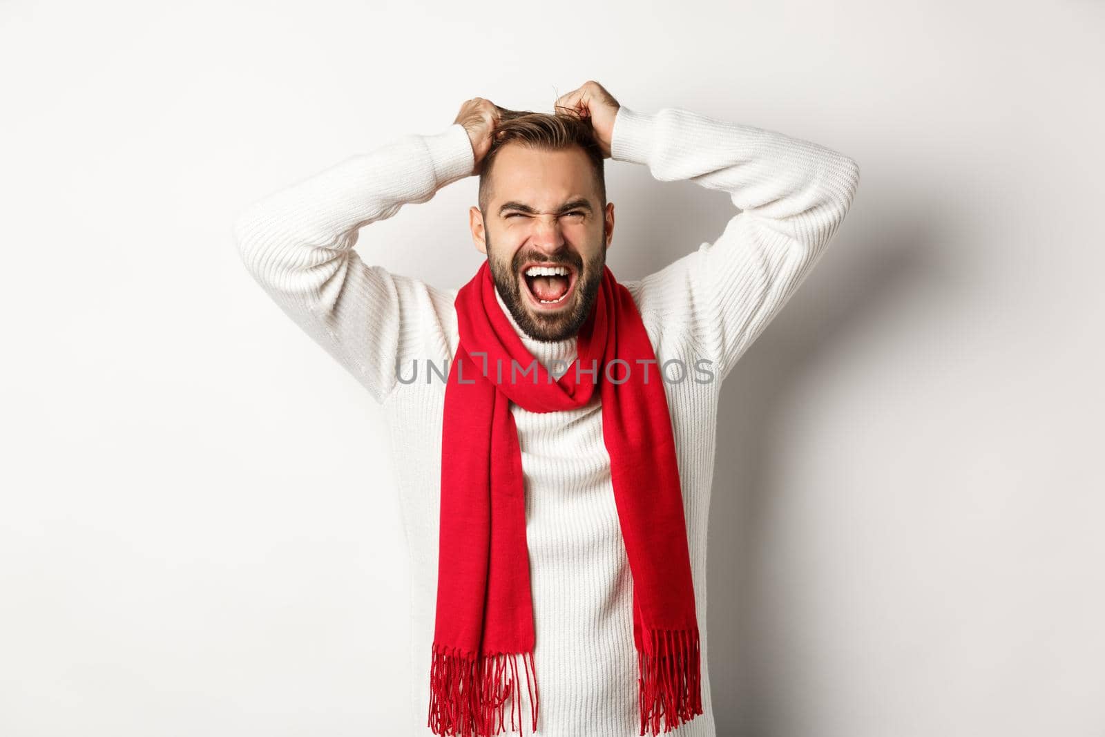 Christmas holidays and New Year concept. Frustrated and angry man pulling hair off head and screaming distressed, standing mad against white background.