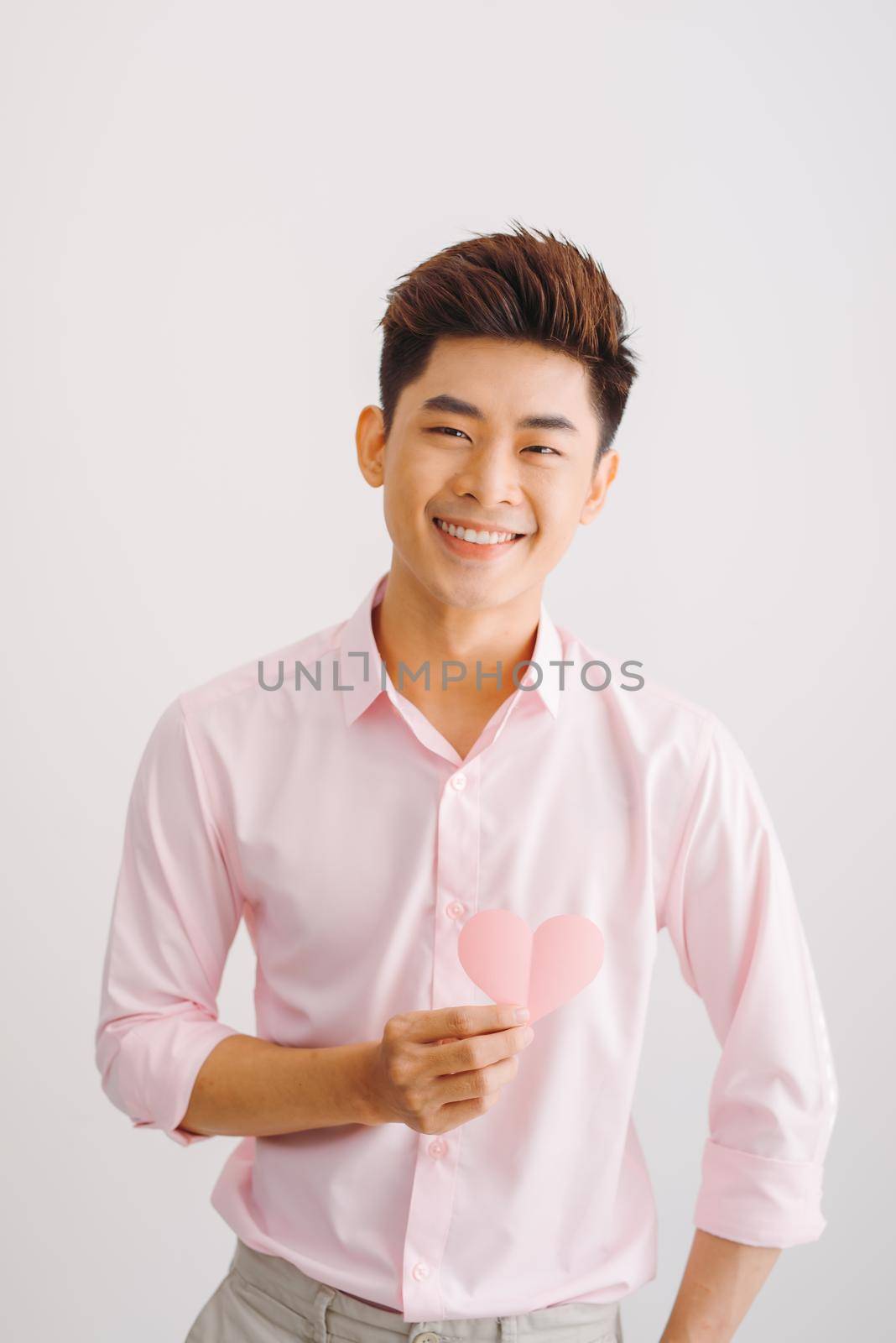 Portrait of tender gentle romantic sweet lovely open-hearted man showing pink heart in hands isolated on white background