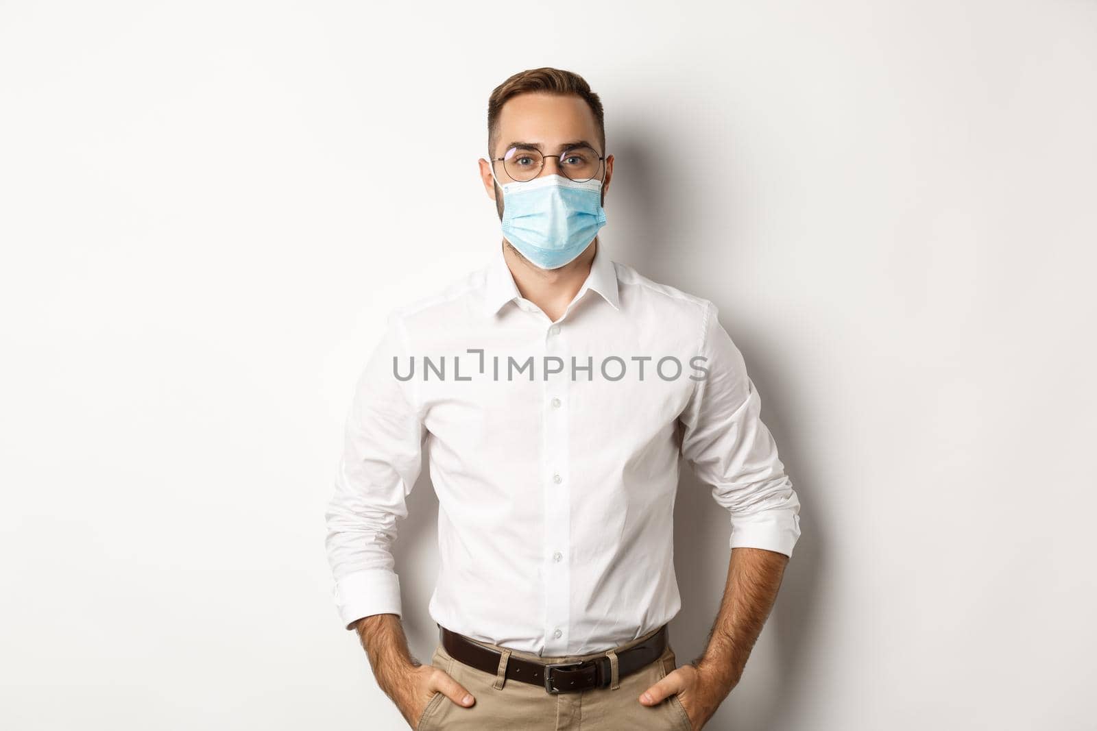Covid-19, social distancing and quarantine concept. Male employee wearing face mask for work, standing against white background.