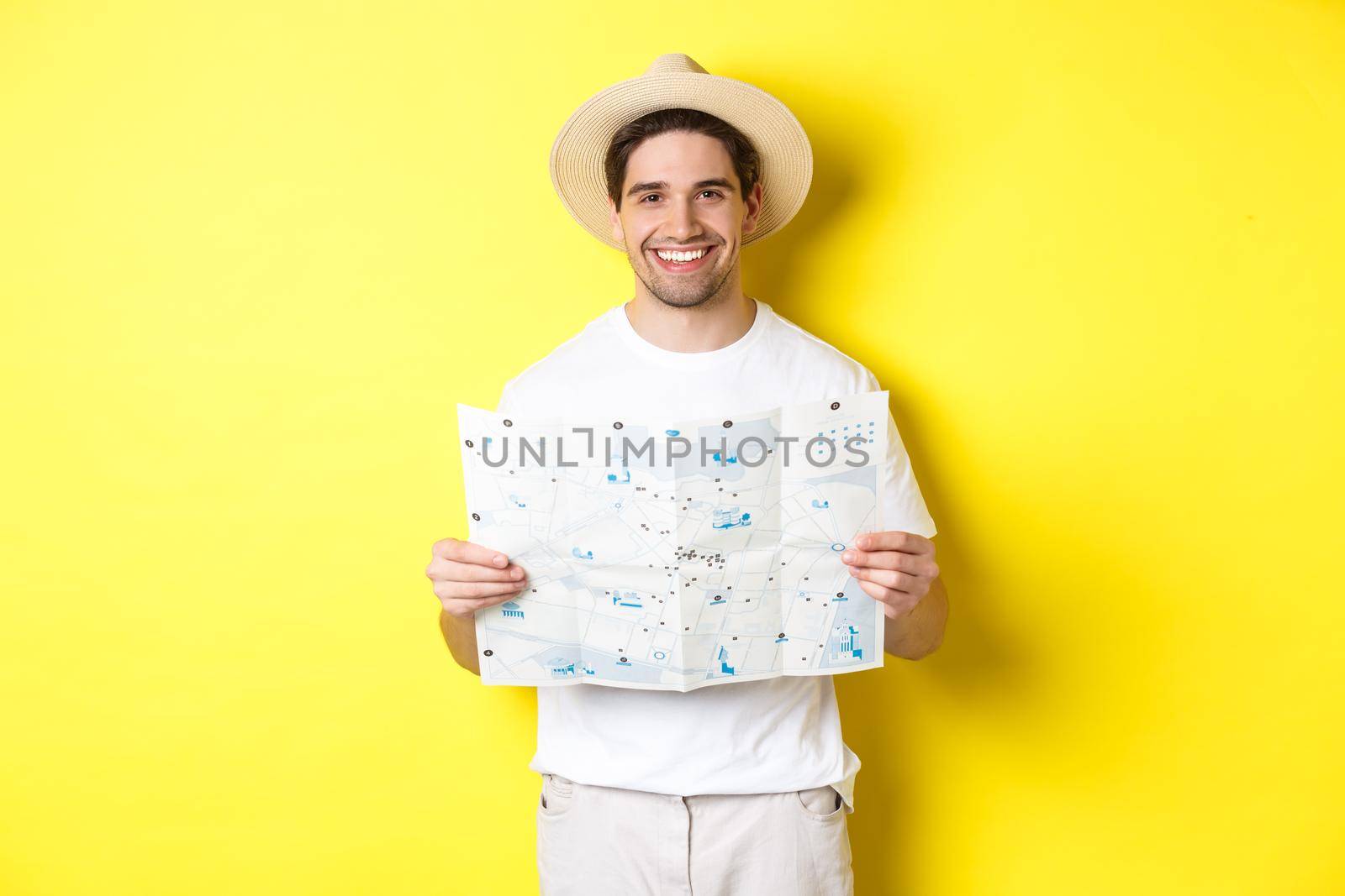 Travelling, vacation and tourism concept. Smiling young man going on trip, holding road map and smiling, standing over yellow background by Benzoix
