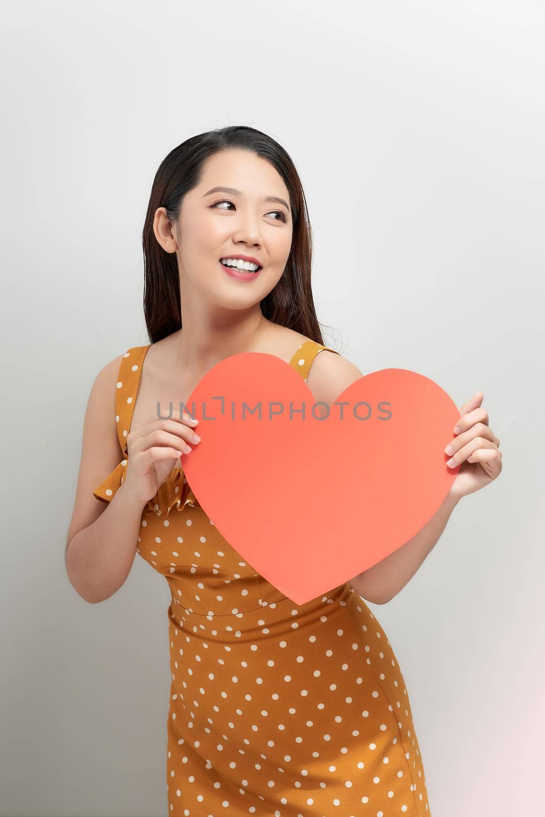 Portrait of attractive asian smiling woman holding red heart on white background by makidotvn