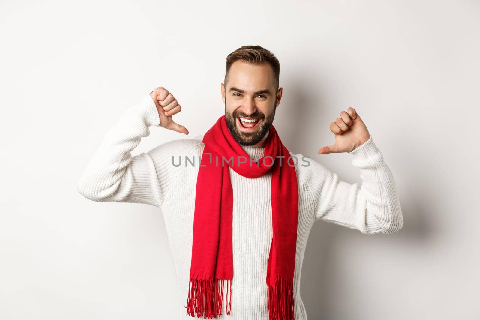 Winter holidays and shopping concept. Confident bearded man pointing at himself and smiling satisfied, celebrating christmas in red scarf and sweater, white background.