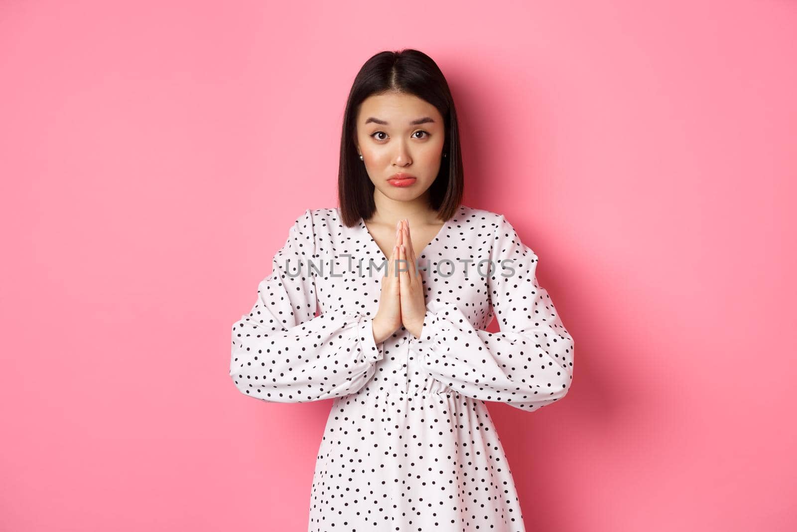Cute asian girl asking for help, begging for favour and looking innocent at camera, pleading against pink background.