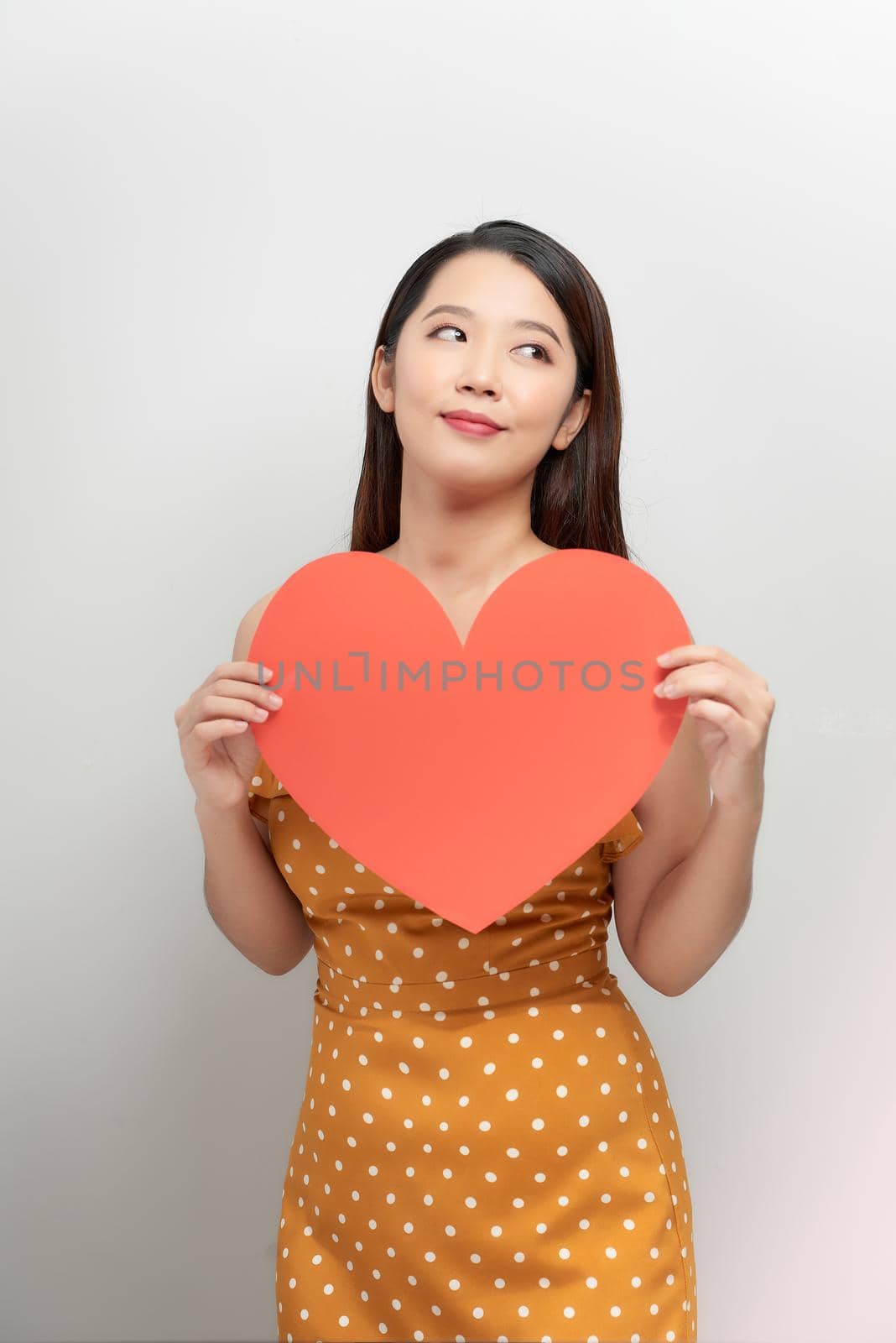 Young asian woman isolated on white wall concept holding heart close-up thinking by makidotvn