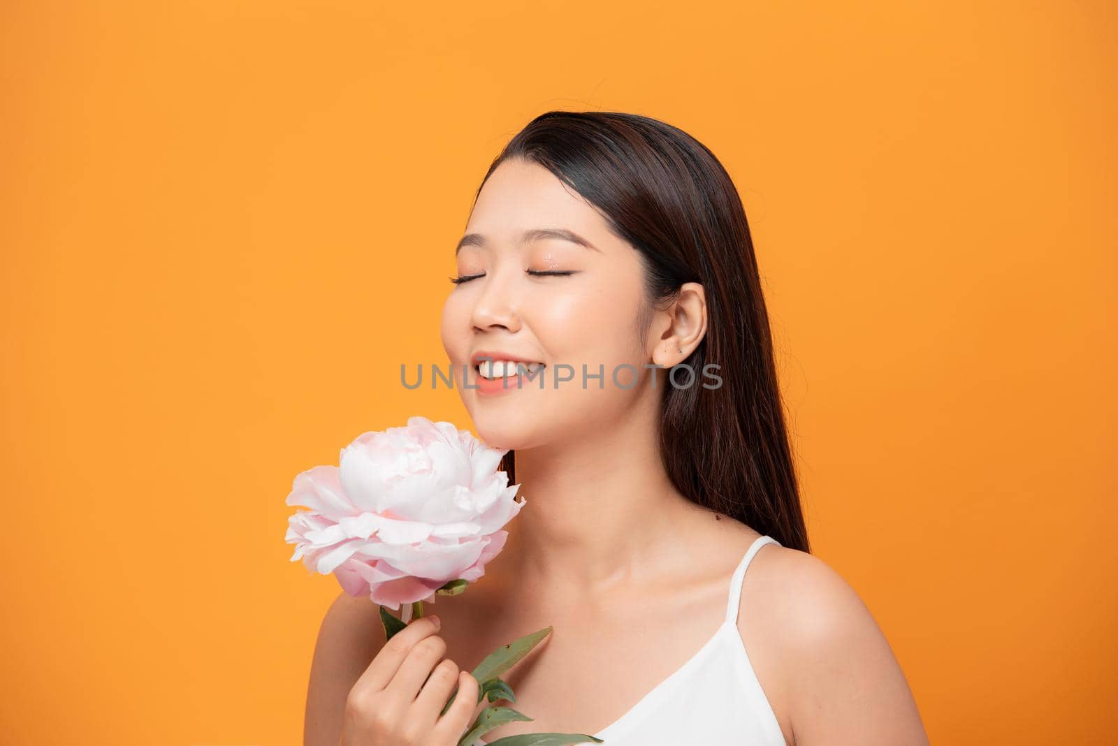 Young woman sniffing pink peony flower closed her eyes on yellow background by makidotvn