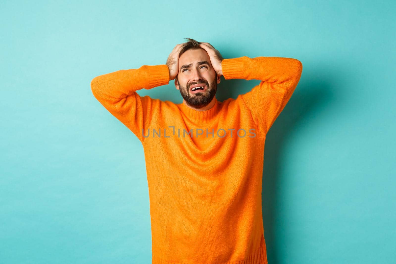 Frustrated and desperate man holding hands on head, looking sad and distressed, standing tensed over light blue background.