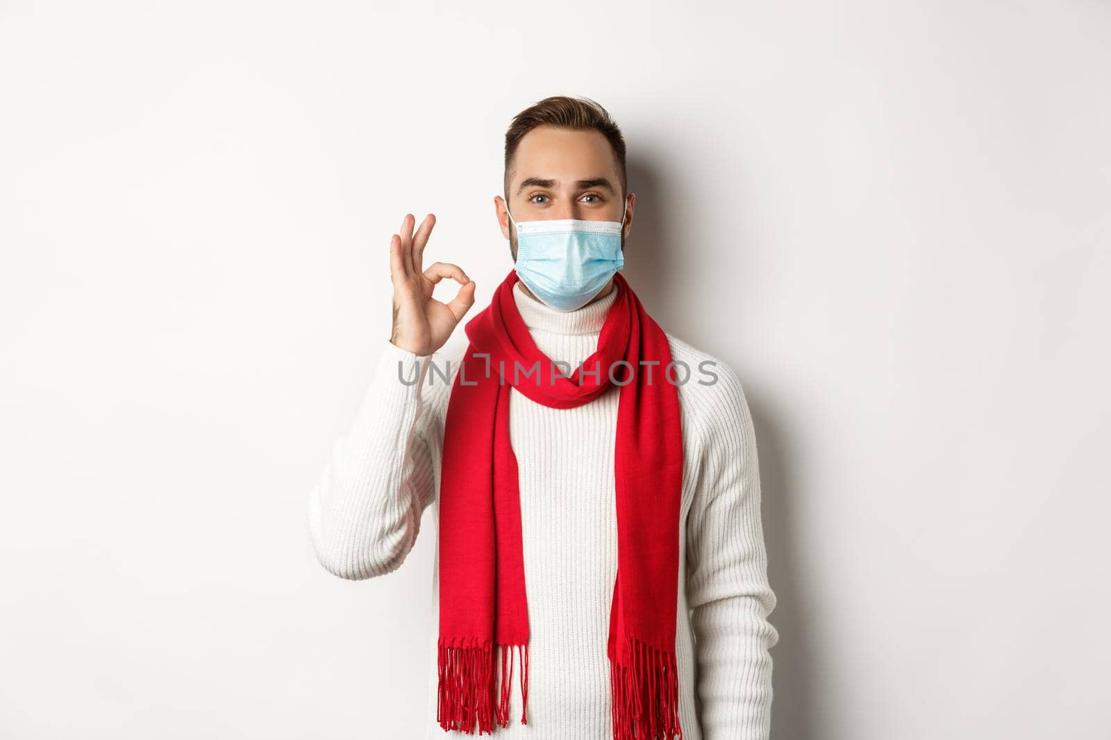 Covid-19, lockdown and quarantine concept. Satisfied handsome guy in face mask showing ok sign, approve or agree, like something, white background.