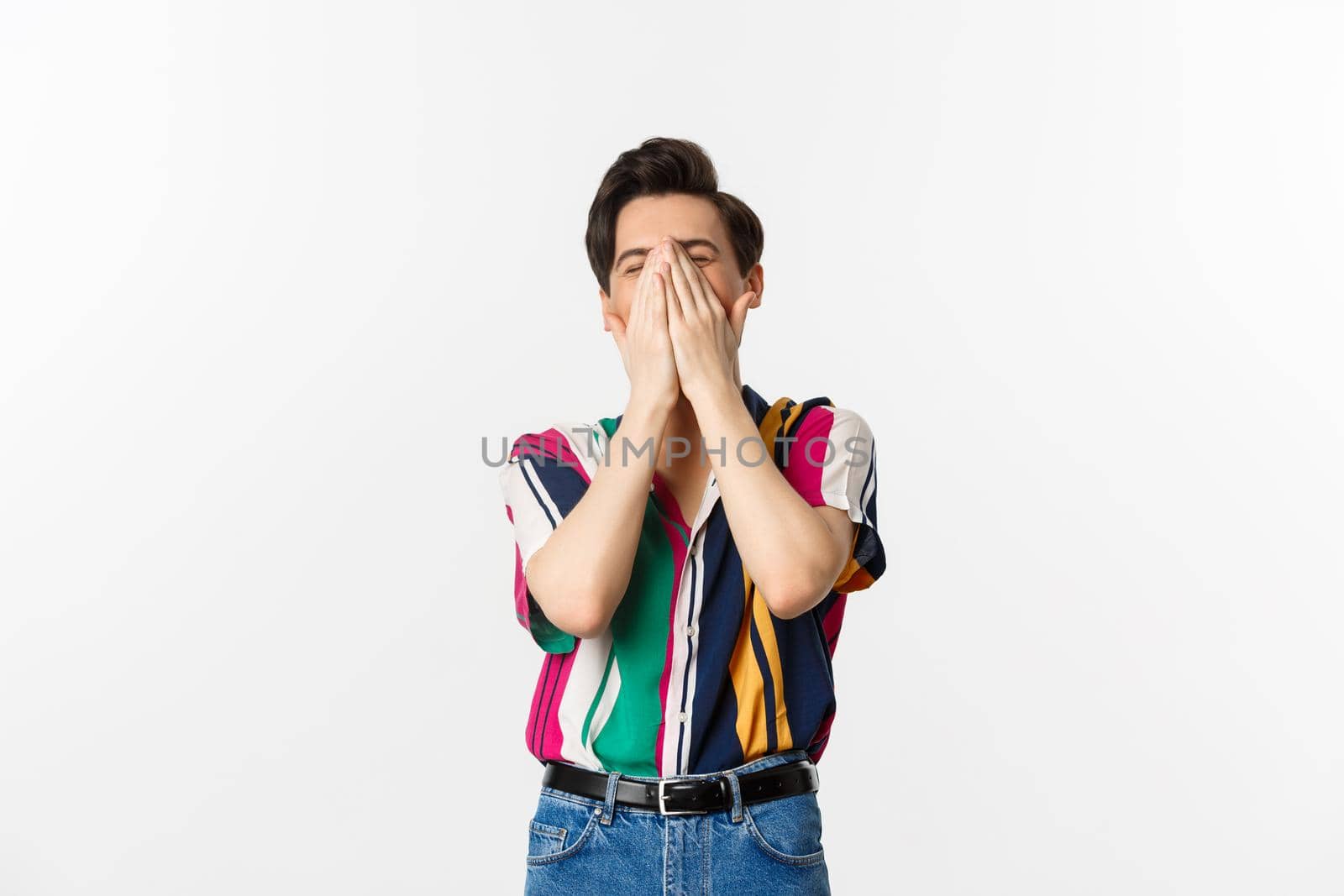 Image of young stylish man sneezing in hands, standing over white background.