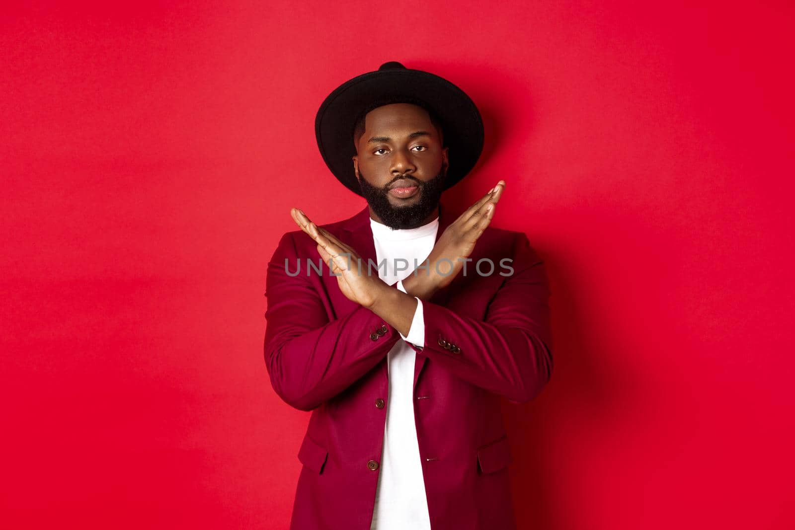 Image of serious Black man strongly disagree, showing cross sign to stop, prohibit something, standing over red background.