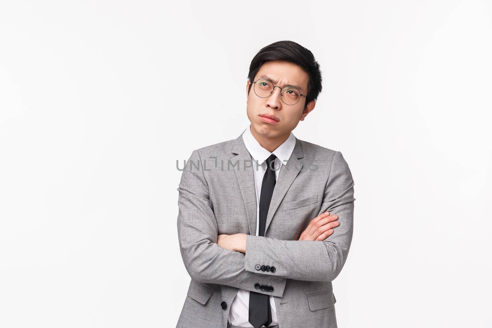 Waist-up portrait of puzzled, serious-looking asian guy in grey suit, looking up frowning and squinting thoughtful, cross hands chest, trying make-up solution, making choice indecisive.