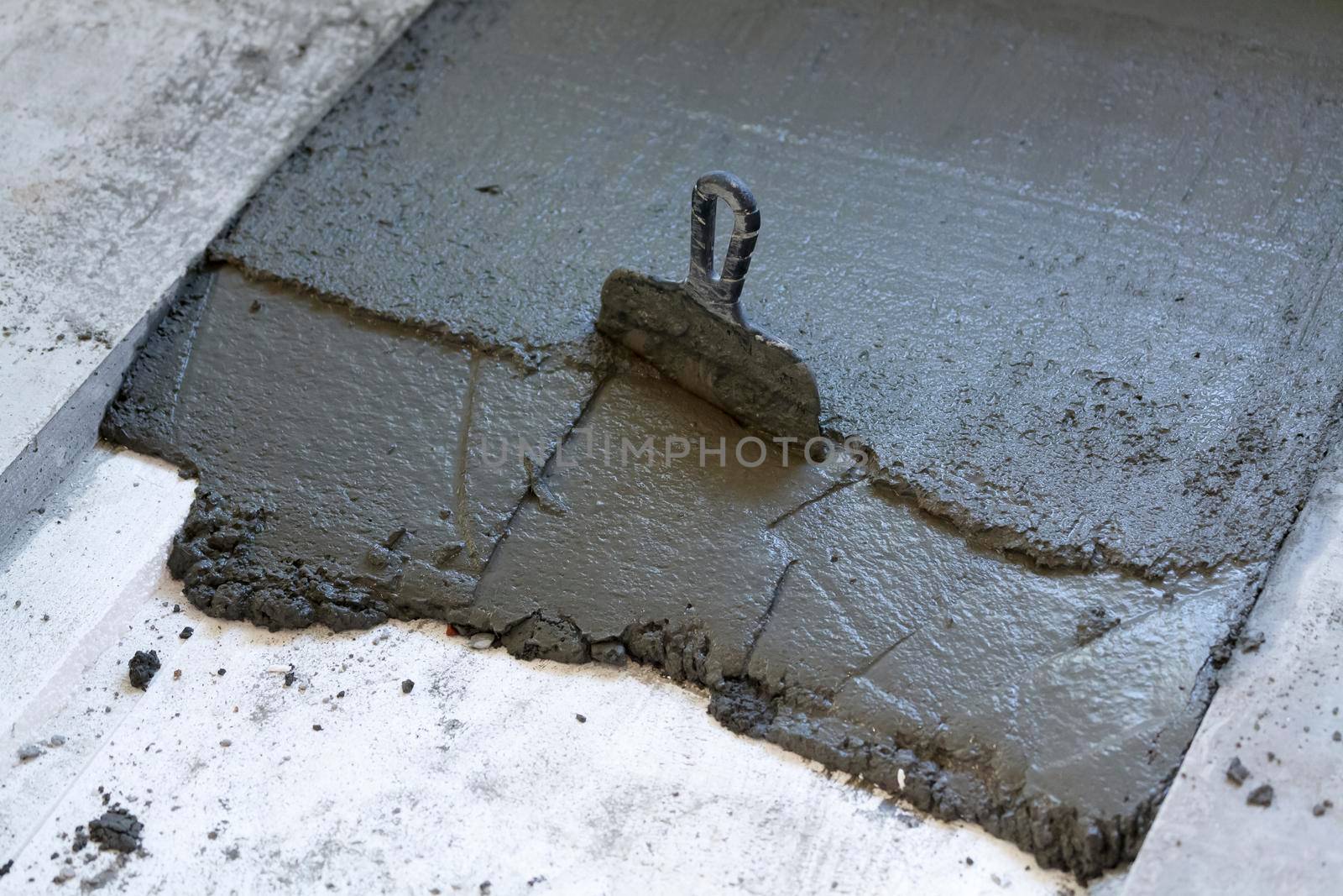 A trowel in a layer of fresh concrete on the floor by Nobilior