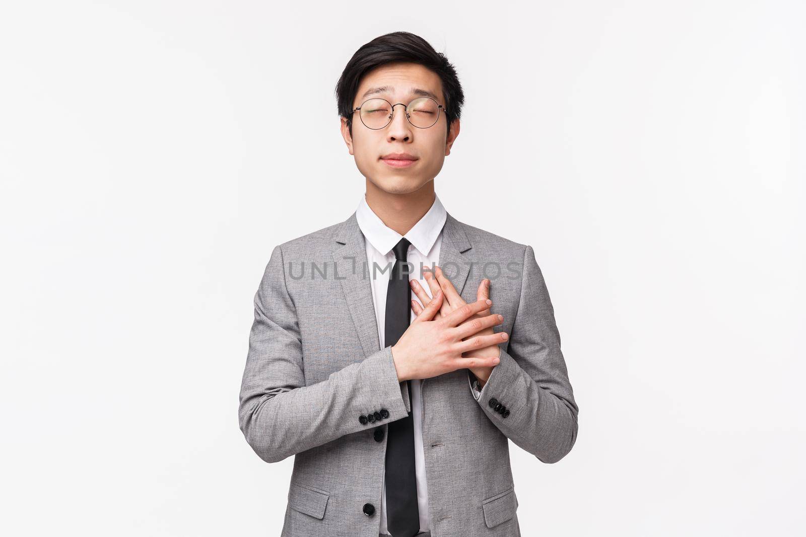 Waist-up portrait of romantic handsome young asian male entrepreneur, office manager have crush on his coworker, hold hands on heart close eyes, daydreaming about falling in love, white background by Benzoix